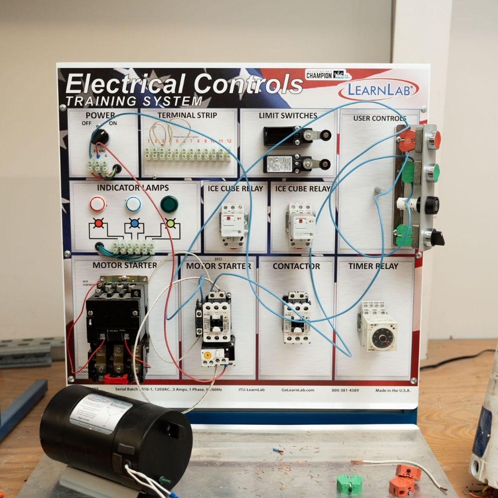 A training board labeled Electrical Controls Training System with various switches, relays, indicator lamps, wires, and electrical components, designed for hands-on learning about electrical control circuits.