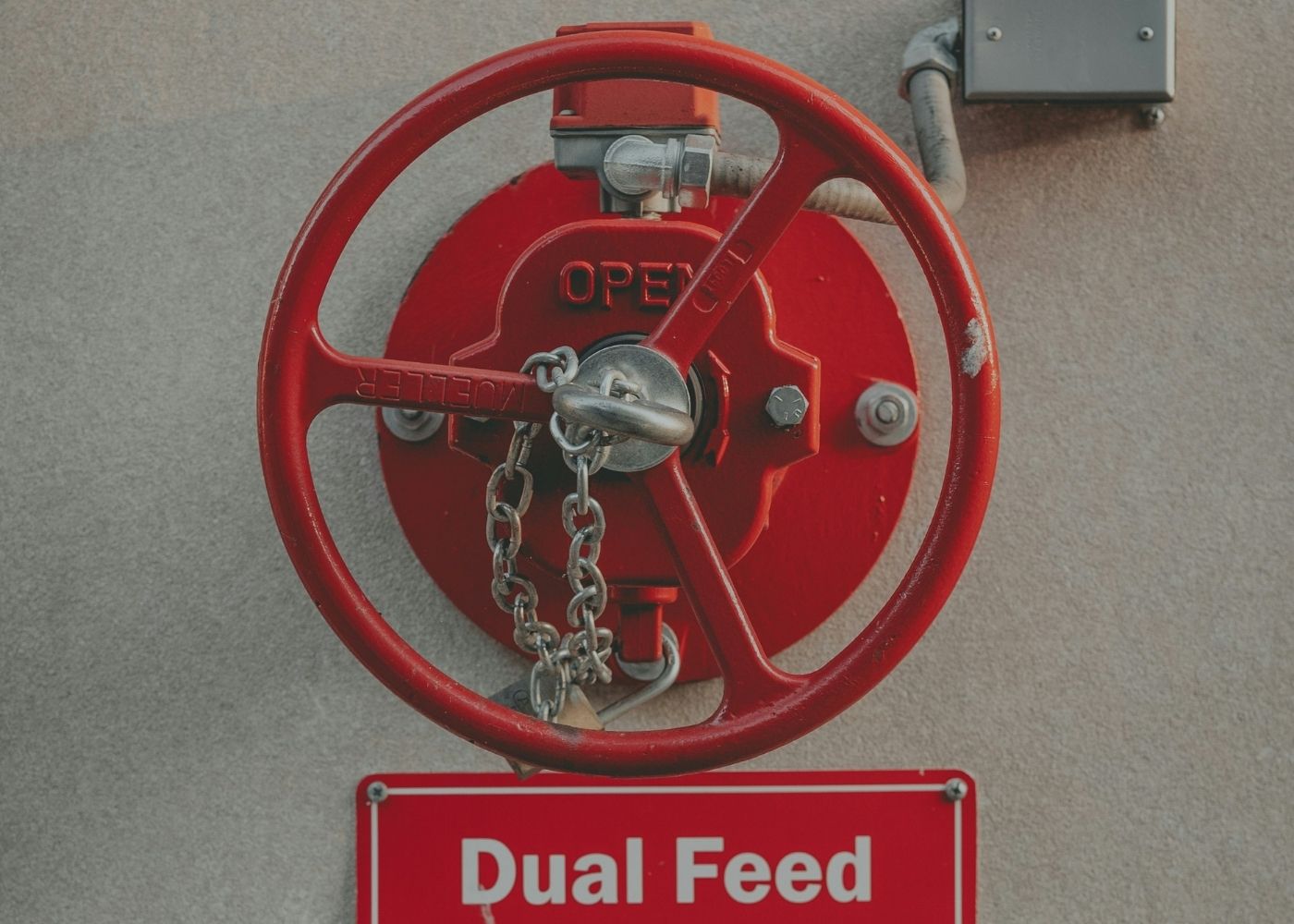 A close-up of a red fire department connection valve and hydrant mounted on a bright yellow wall, with a shadow cast to the right and a window partially visible in the background.
